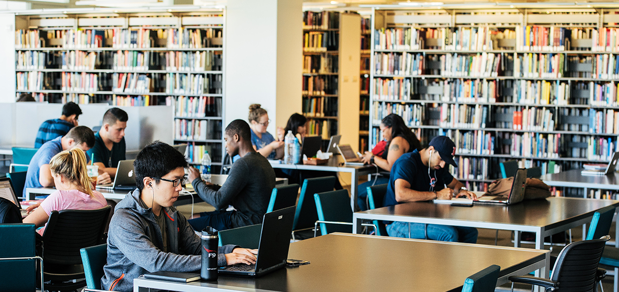 Students sitting at different tables and studying in the library.