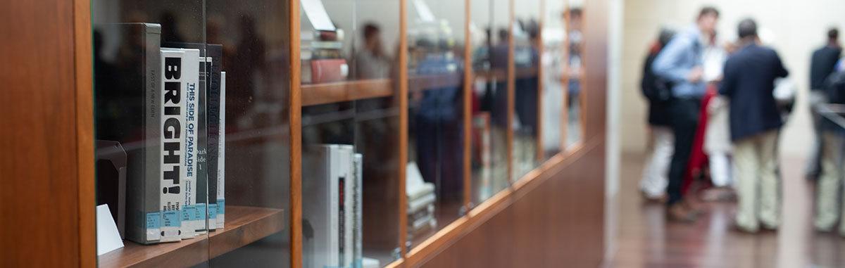 Closeup on books in glass cabinet with people in background
